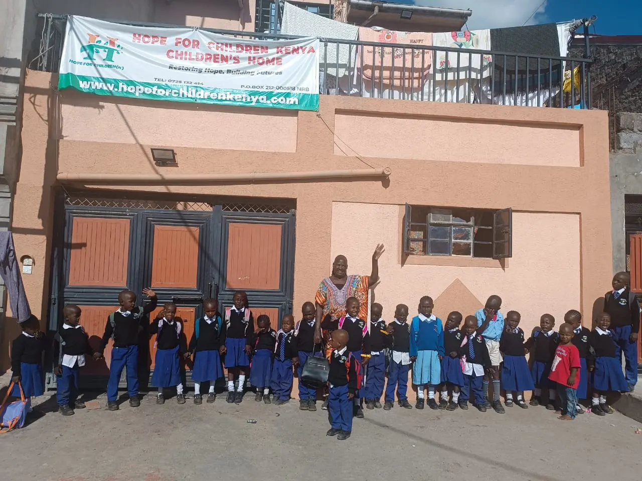 Children in school uniforms lined up with a caregiver in front of the Hope for Children Kenya children's home